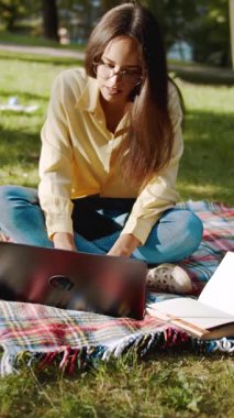 Parkta dizüstü bilgisayarıyla çalışan bir kadın güneşli havanın ve doğanın tadını çıkarıyor.