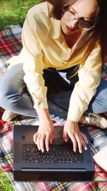 Bir kadın güneşli bir günde dizüstü bilgisayarını kullanarak parkta ders çalışmaktan zevk alır ve sakin bir öğrenme ortamı yaratır.