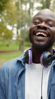 Parkta, kulaklık takıp güneşlenirken neşeyle gülen bir adam.