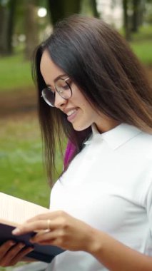 Bir kadın, etrafı gezerken parkta huzur içinde yürüyüp kitap okumaktan zevk alır.