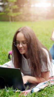 Bir kadın güneşli bir öğleden sonra çimlerde uzanırken dizüstü bilgisayarında çalışmaktan zevk alır.