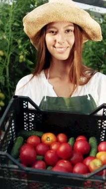 Genç bahçıvan canlı bitkilerle dolu bir serada taze domates tutarken gülümsüyor.