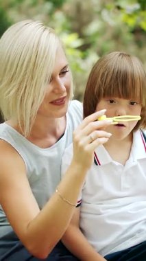 Neşeli bir çocuk, güneşli bir parkta gülümseyen bir yetişkinin yanında kabarcıklarla oynar ve eğlenceli bir atmosfer yaratır.