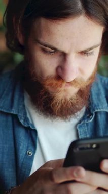 Kafedeki bir adam, vaktinin tadını çıkarırken rahat yerinde mesajlaşan akıllı telefonuna odaklanır.