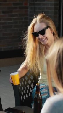 Dostlar, güneşli bir günde açık havada içki içerken rahatlar ve sohbet ederler.