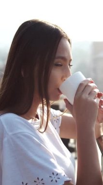 Bir kadın sabah kahvesini balkonda içer güneş ışığında ıslanır ve temiz havada dinlenir.