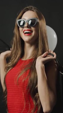 Şık bir kadın alışverişçi kırmızı bir alışveriş çantası ve düşen balonlarla poz verir.