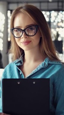 Kendine güvenen bir iş kadını ofisinde elinde bir pano tutarken gülümsüyor.