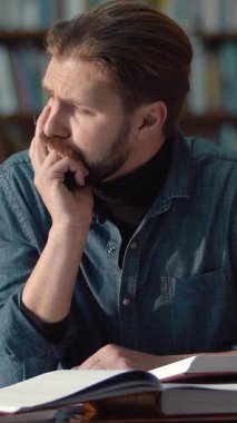 Bir öğrenci kütüphane kitaplarını sessiz bir yerde inceler ve derinden düşünür.