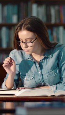 Bir kadın öğrenci gündüz vakti sessiz bir kütüphanede derslerine odaklanır.