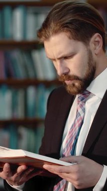 Resmi giyinmiş bir adam sessiz bir kütüphane ortamında kitap okumaktan hoşlanır.