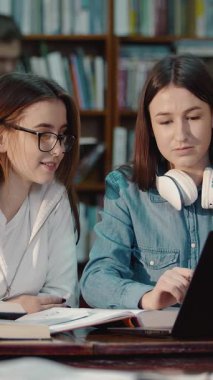 İki öğrenci kütüphane ortamında fikirleri paylaşıyor ve birlikte okuyorlar.