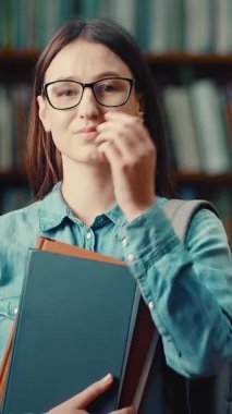 Kütüphanedeki bir kadın öğrenci elinde bir kitap tutarken neşesini paylaşıyor.