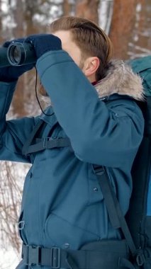 Yürüyüşçü, karlı bir ormanda vahşi yaşamı tespit etmek için dürbün kullanır. Kışın güzelliğini keşfeder.