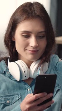 Kadın kanepede oturup kulaklıklı bir akıllı telefondan müzik dinliyor.