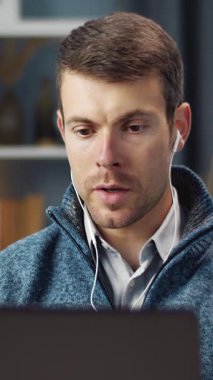 Adam evde oturuyor, dizüstü bilgisayar kullanıyor ve kulaklıkla dinliyor..