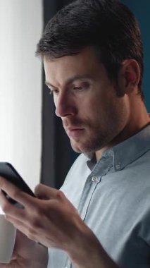 Adam elinde bardak tutarken akıllı telefon ekranına bakıyor..