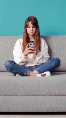 Bir kız evde dinlenirken akıllı telefonunu kullanarak kanepede oturuyor..