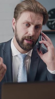 Bir iş adamı masasında dizüstü bilgisayarla çalışırken telefonla meşgul oluyor..