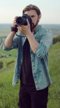 Bir adam fotoğrafçı yeşil çimlerin üzerinde duruyor, şehirden uzakta bir kamerayla fotoğraf çekiyor..
