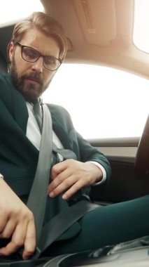 Araba kullanırken takım elbiseli bir adam emniyet kemerini bağlar..