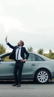 Takım elbiseli adam kırsal alanda park halindeki bir arabanın yanındaki ağı aramak için akıllı telefon kullanıyor..
