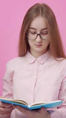 Pembe gömlekli bir kadın, hikayeye dalmış pembe bir alanda mavi bir kitap okuyor..