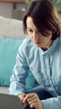 Kadın rahat bir ev ortamında dizüstü bilgisayar kullanarak kanepeye oturur..