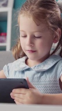 Genç kız tablet kullanarak evde oturuyor, gülümsüyor ve ekrana odaklanıyor..