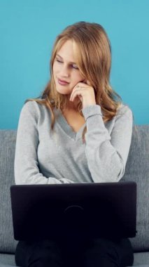 Bir kadın dizüstü bilgisayarla gri bir koltukta oturuyor, derin düşüncelere dalmış ve hafifçe gülümsüyor..