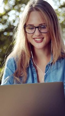 Bir kadın gün içinde parkta dizüstü bilgisayarla çalışırken gülümsüyor..