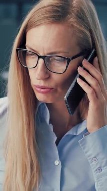 Bir kadın, kapalı alanda konuşurken, akıllı telefonuyla odaklanmış bir şekilde konuşur..