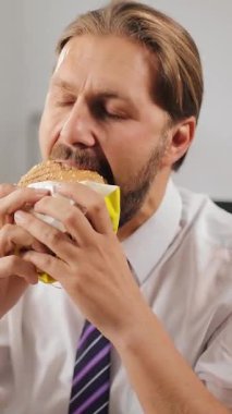 Adamın biri ofis ortamında mola verirken hamburgeri ısırıyor..