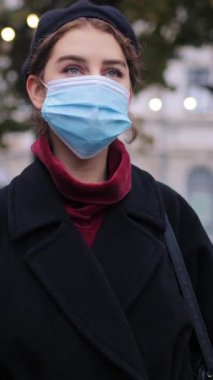 Kadın açık havada şapkasını düzeltirken mavi bir maske takıyor..