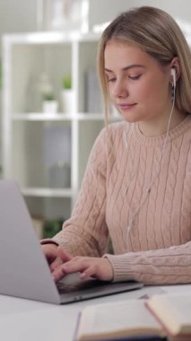 Kadın, bitkilerle dolu parlak bir odada dizüstü bilgisayar kullanarak masada oturuyor..