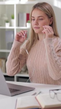 Kulaklıklı bir kadın öğrenci evde dizüstü bilgisayarla çalışıyor, odaklanmış görünüyor..