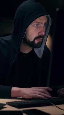 Bir adam gece loş bir odada dizüstü bilgisayarda ciddi bir şekilde yazı yazıyor..