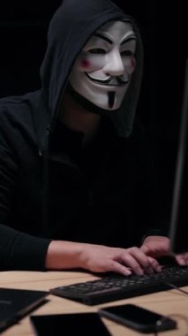 Adam karanlık odada dizüstü bilgisayarda yazıyor. Maske takıyor ve yoğun odaklı bir başlık takıyor..