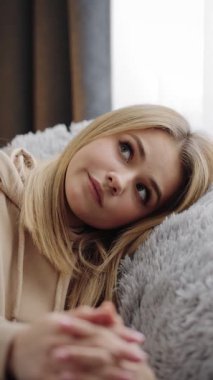 Kanepede oturan kadın, düşüncelere dalmış, yumuşak ışıklandırmalı rahat bir evde..