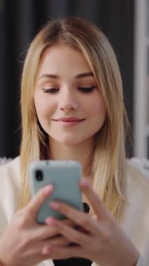 Kadın parlak bir odada oturuyor ve gülümserken akıllı telefonuyla mesaj atıyor..