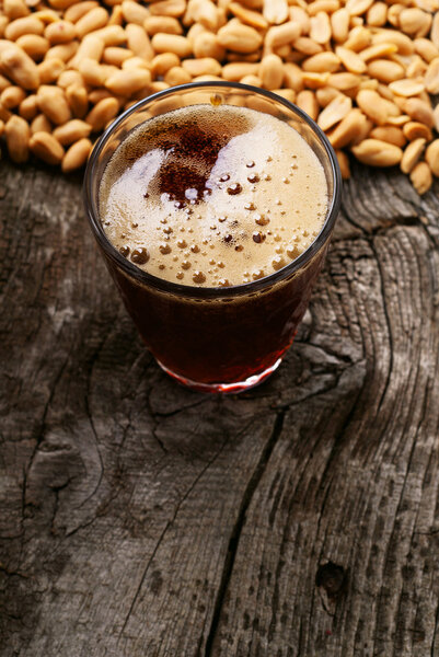 glass of dark foamy beer with snack to beer peanuts
