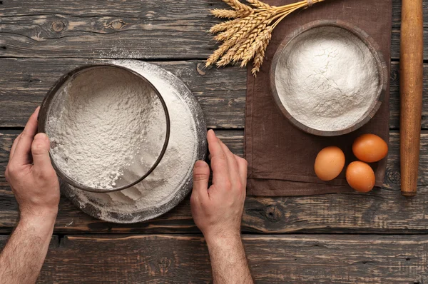 Baker Sift mąkę na ciemnym rustykalnym drewnianym tle — Zdjęcie stockowe