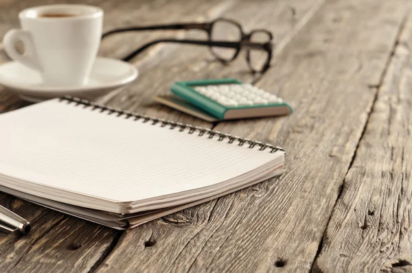 Blocco note aperto con penna, tazza di caffè, calcolatrice e bicchieri — Foto Stock