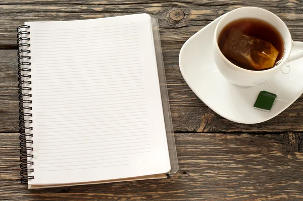 Cuaderno abierto con páginas en blanco con taza de té negro —  Fotos de Stock