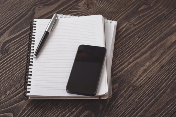 ノートブックと木製の暗い背景に黒いスマートフォン — ストック写真