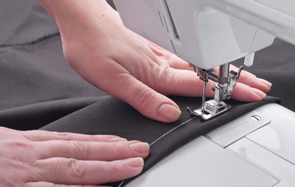 Женские руки с тканью у швейной машинки
