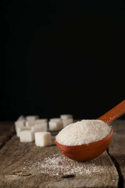 Açúcar branco em uma colher de madeira e cubos de açúcar — Fotografia de Stock