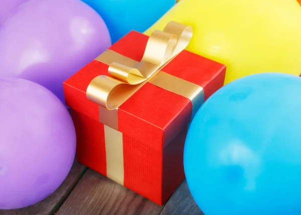 Rode geschenkdoos met gouden lint in ballonnen — Stockfoto