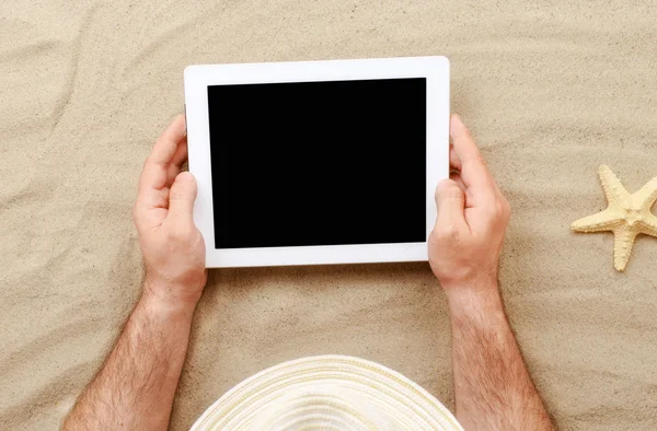 Man holding tablet with blank screen lying on the beach — Stock Photo, Image