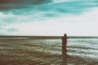 Gün batımında denizde yürüyen genç kadın silüeti